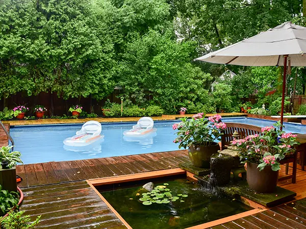 Luxury backyard swimming pool with floating loungers, surrounded by lush greenery, a koi pond, and vibrant flowers.